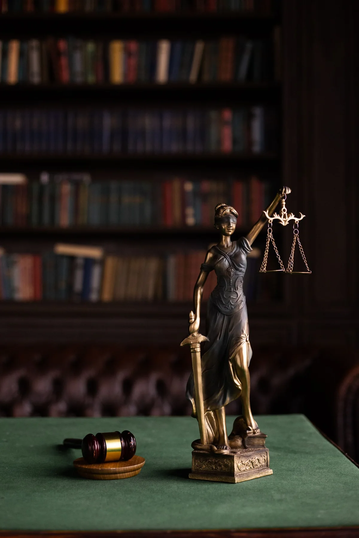 Kitap raflarının önünde adalet terazili Themis heykeli ve ahşap tokmak.